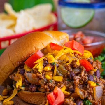 A Taco Joes sandwich piled high with saucy taco beef, melted cheddar, and diced tomatoes on a soft bun.