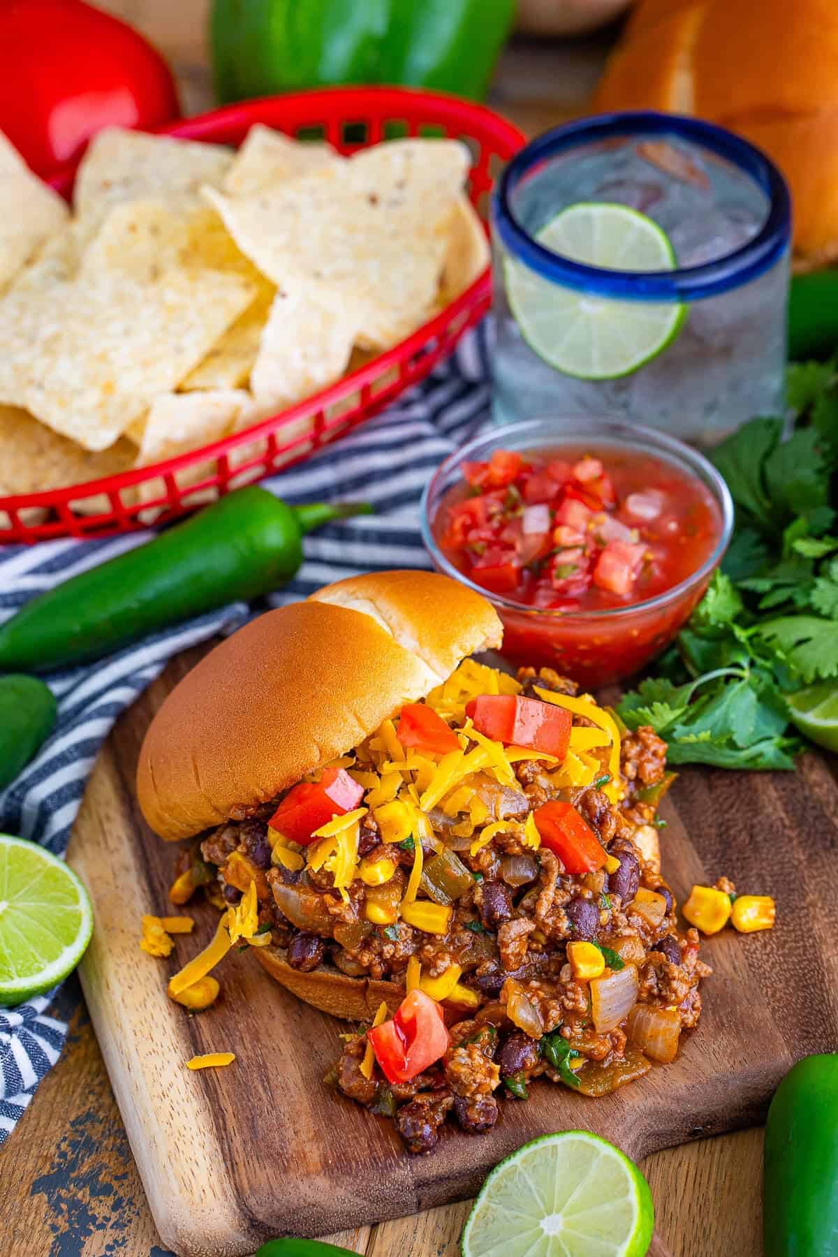 Taco Joes served on a wooden board with tortilla chips, salsa, jalapenos, and lime.