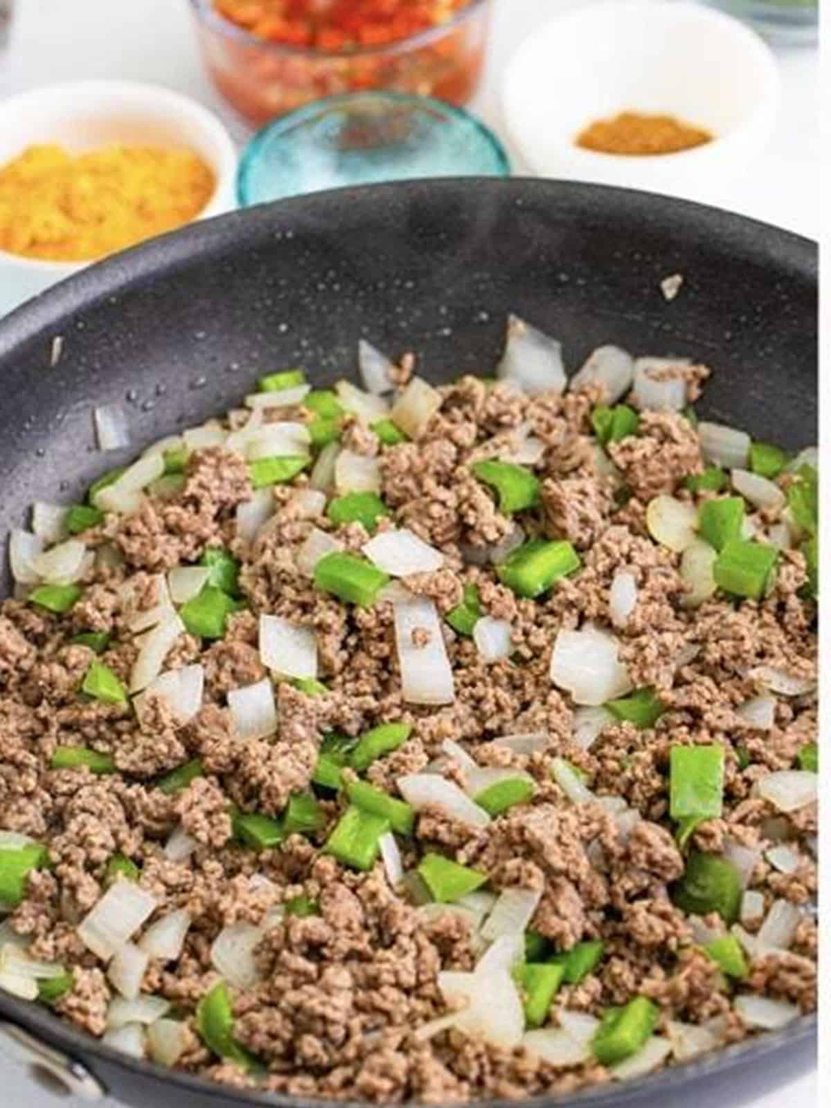 Browning ground beef with diced onion and green bell pepper in a skillet for Taco Joes.