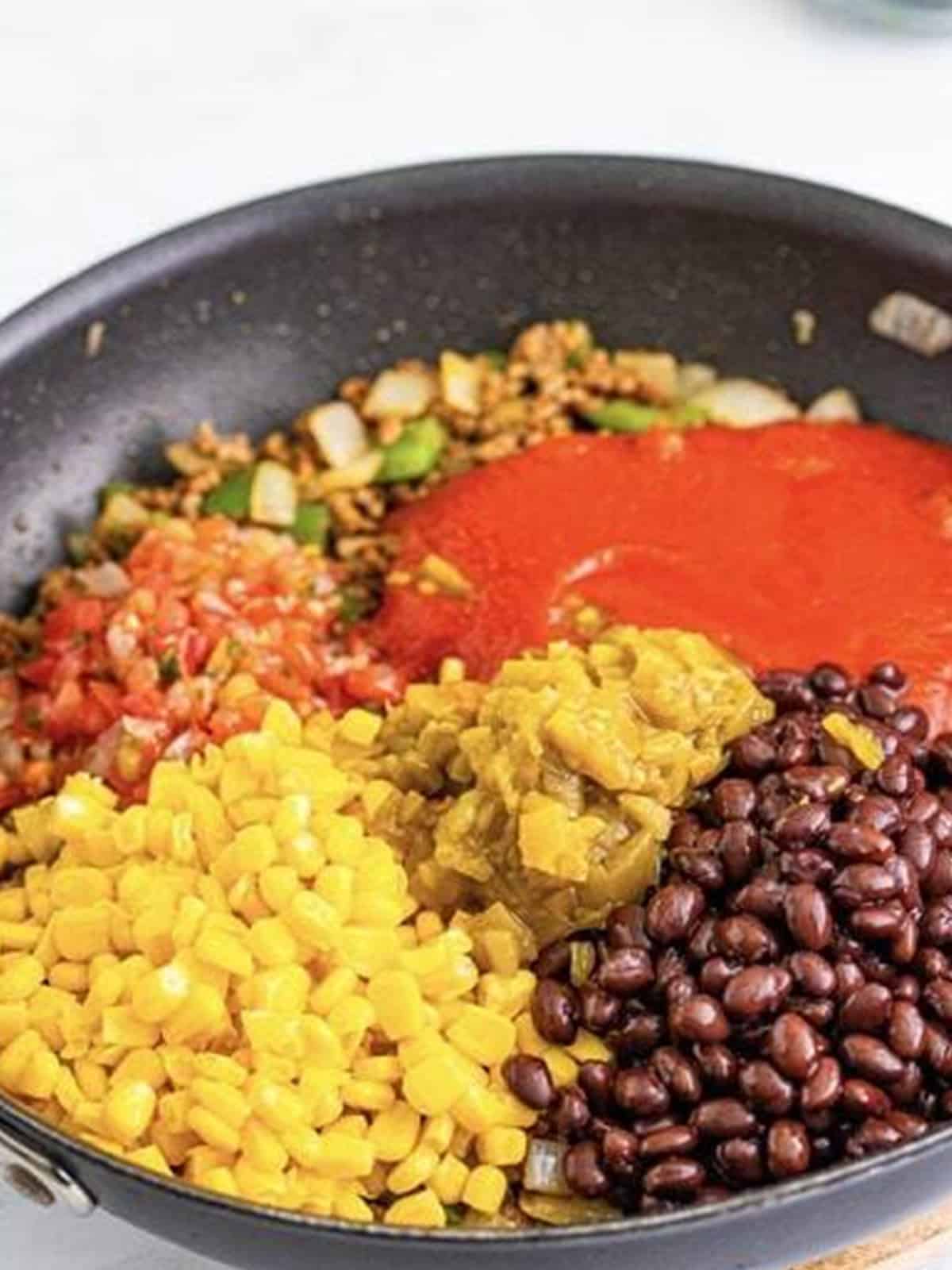 Adding tomato sauce, salsa, black beans, corn, and green chiles to the skillet for Taco Joes.
