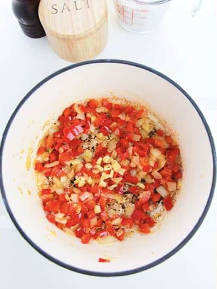 Diced onion, garlic, red bell pepper, and ginger sauteing in a white pot for Thai Red Curry Soup.