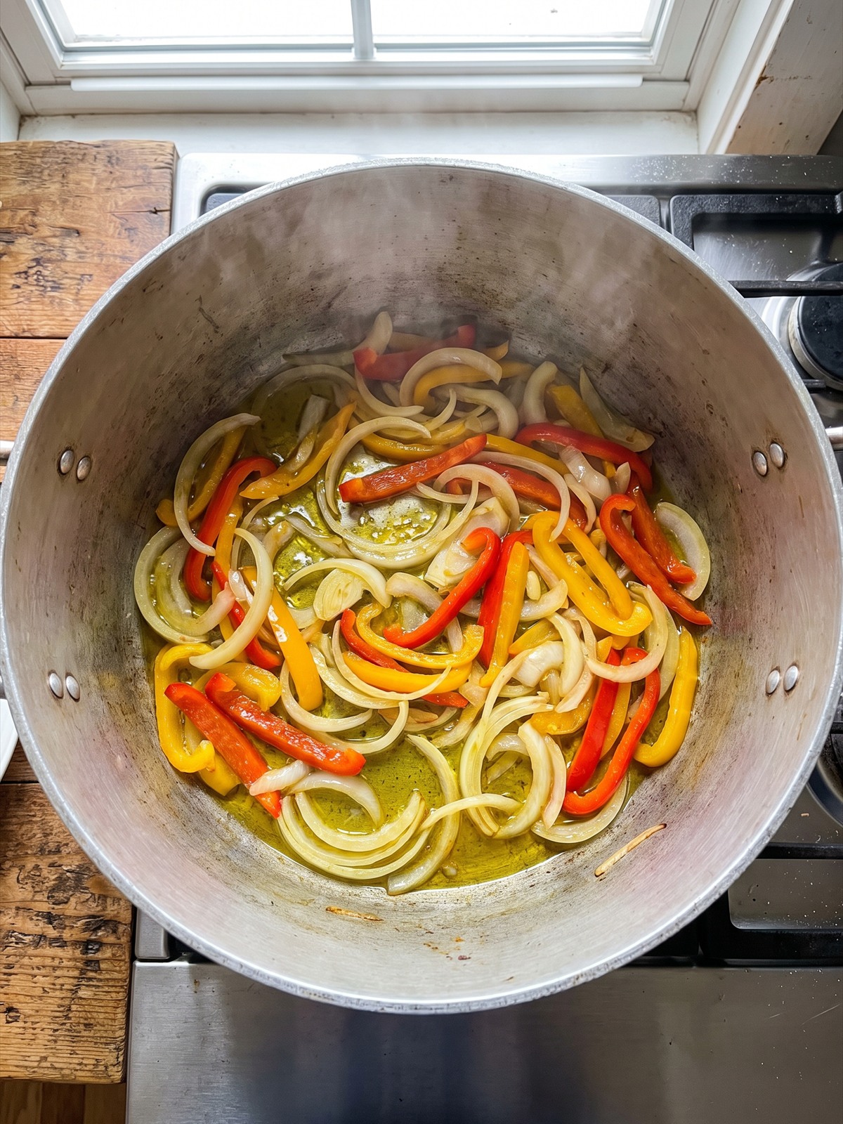 Sliced onion and bell peppers softening in a pot.