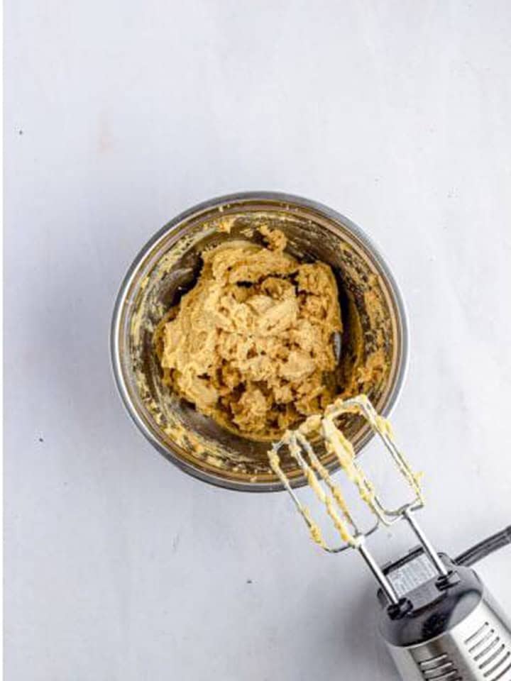 Butter, brown sugar, egg yolk, and vanilla mixed together in a glass bowl with a hand mixer for toffee bars.