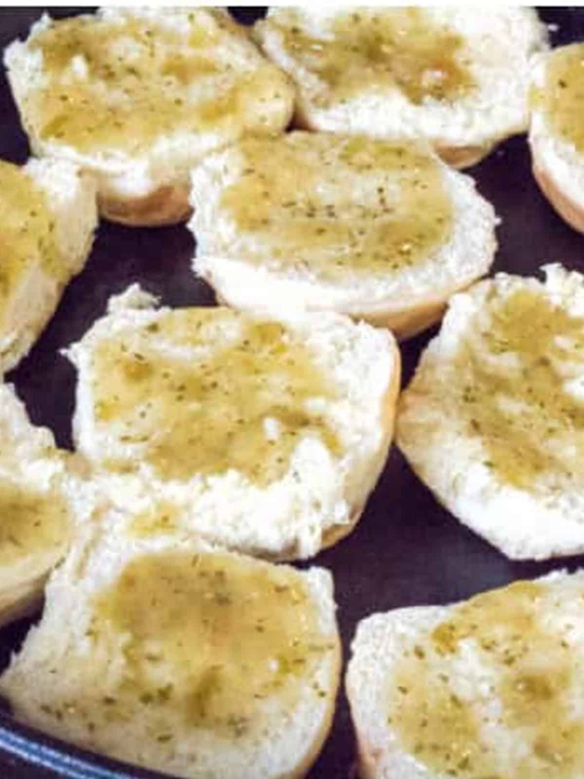 Slider roll bottoms brushed with salsa verde in a cast iron skillet.