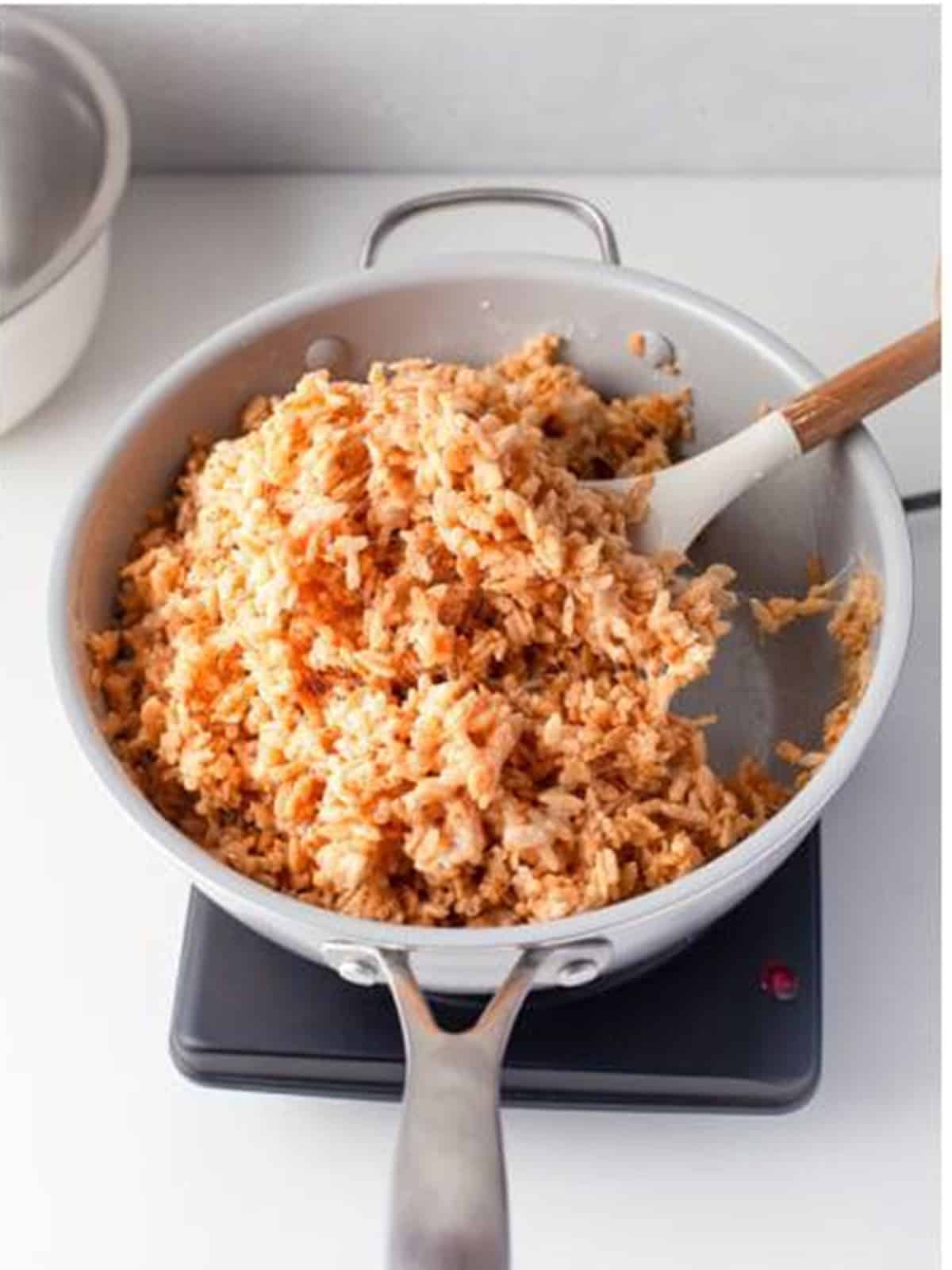 Rice Krispies cereal stirred into the melted marshmallow mixture in a saucepan.
