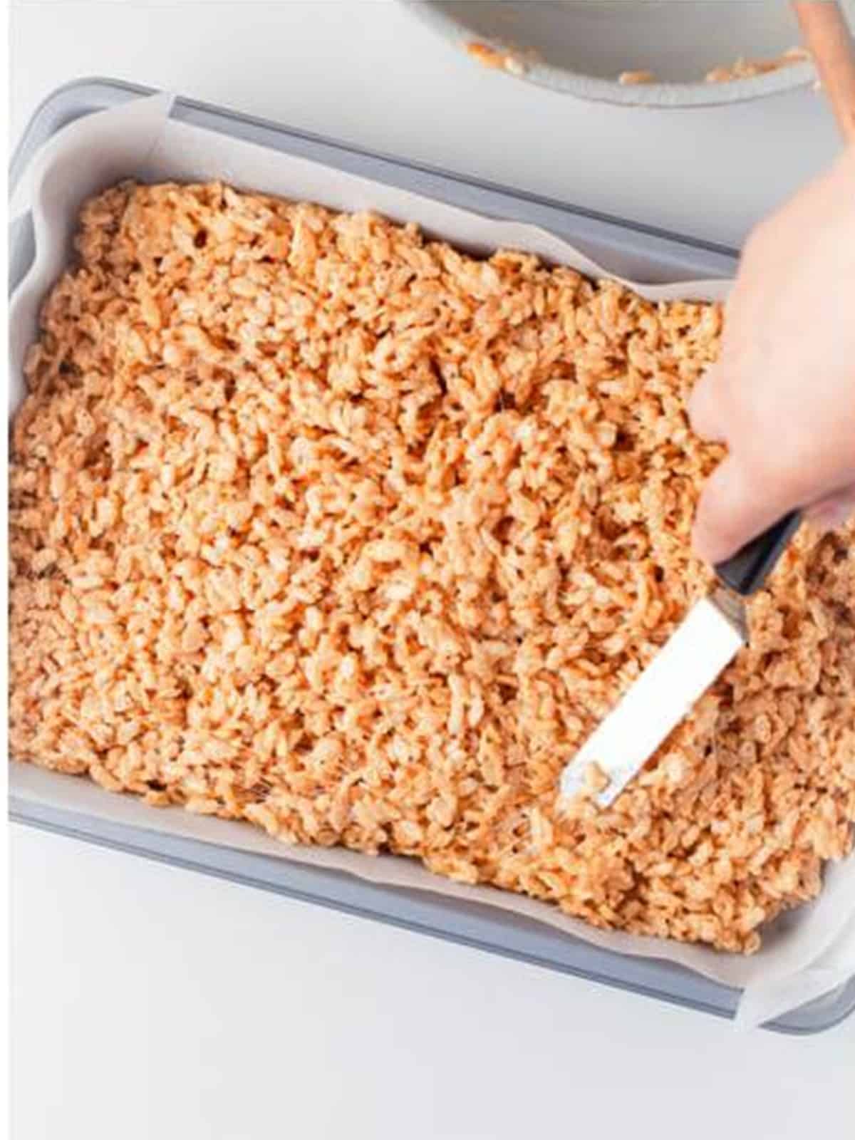 Rice krispie mixture pressed evenly into a parchment lined 9x13 baking pan with a spatula.