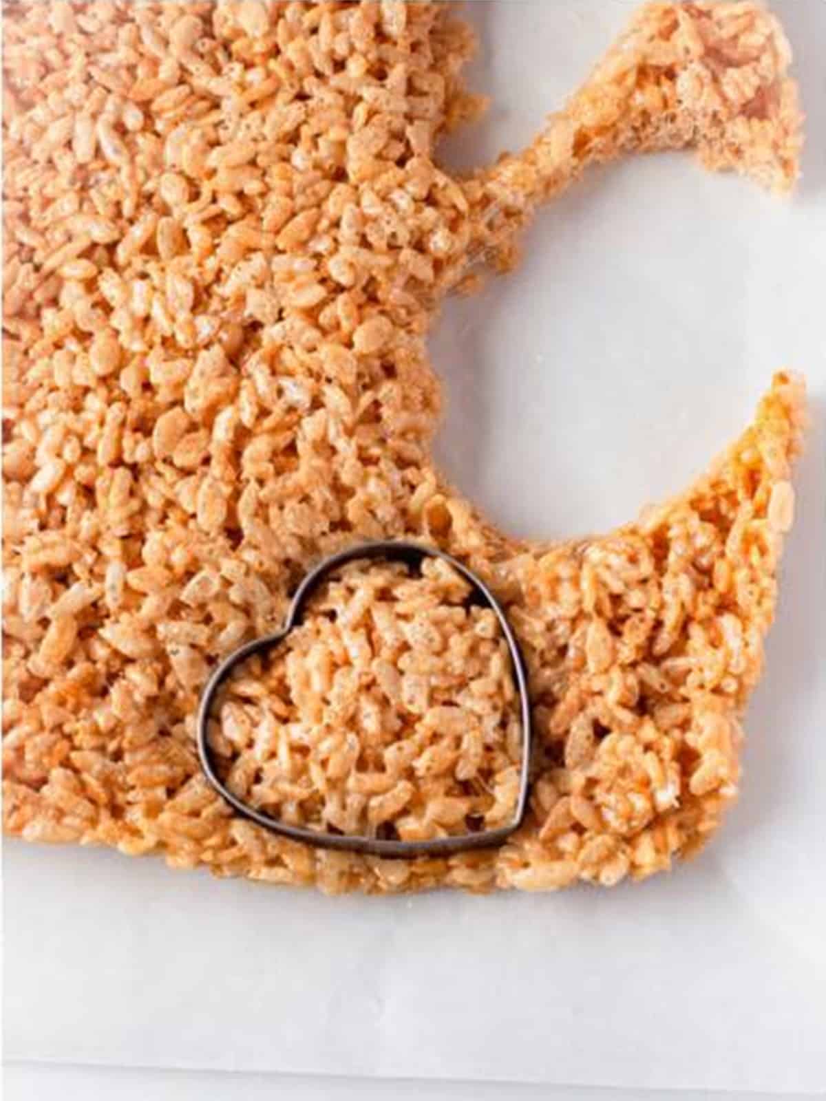 Heart shaped cookie cutter cutting hearts out of the slab of rice krispie treats.