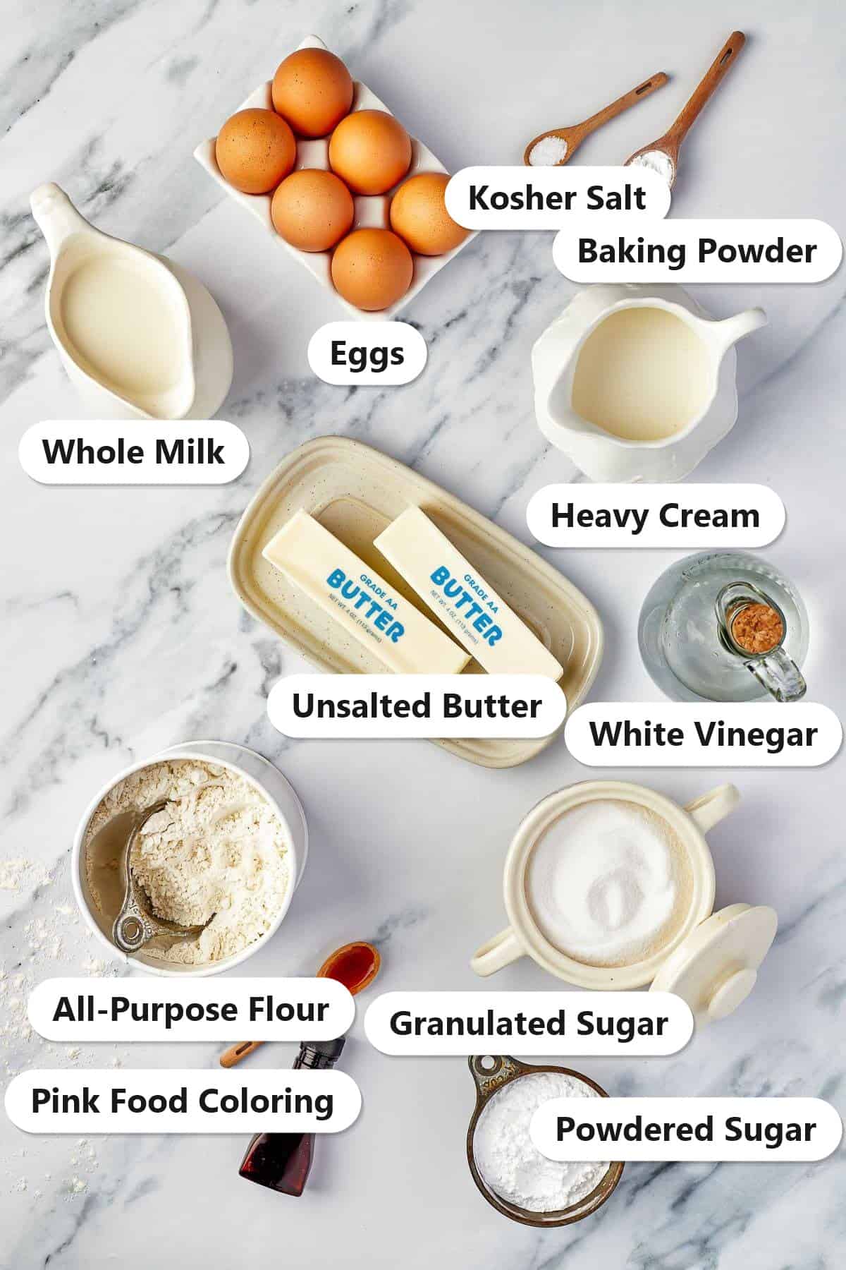 Labeled ingredients for Valentines Day Cupcakes including butter, sugar, eggs, whole milk, heavy cream, flour, baking powder, vinegar, powdered sugar, and pink food coloring.