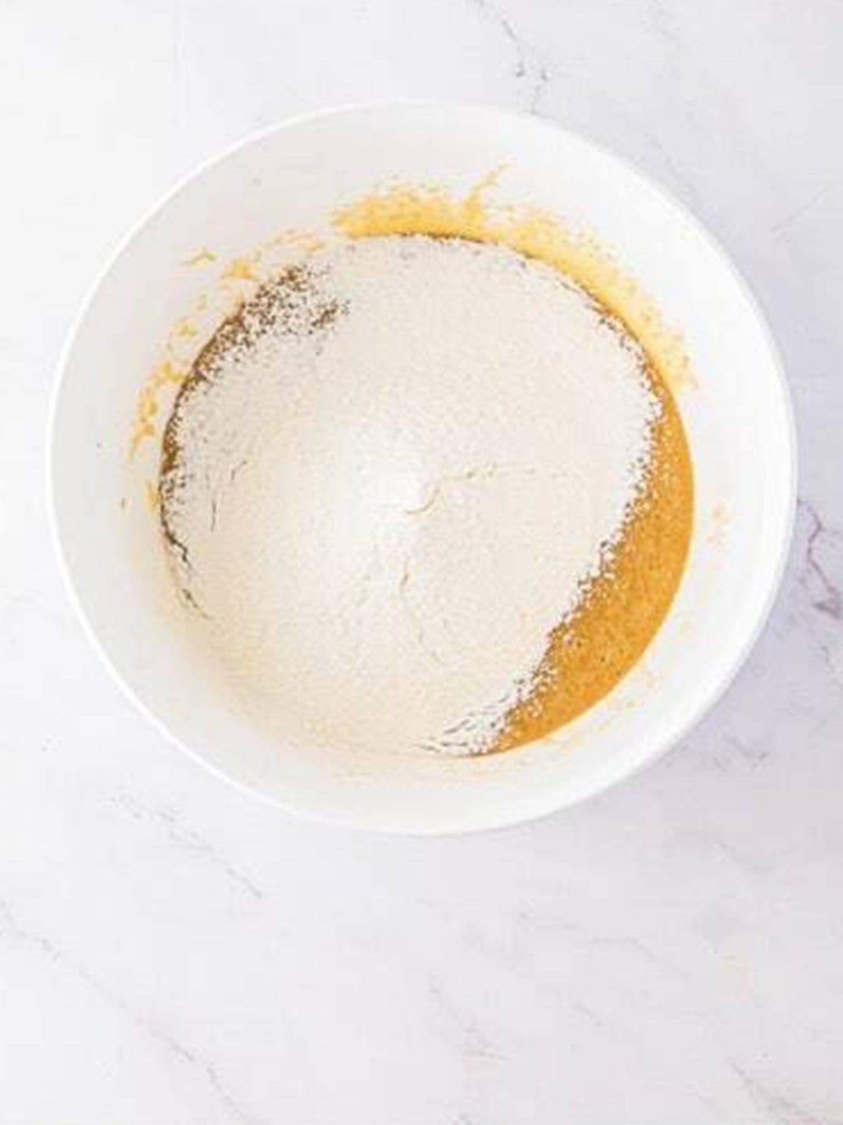 Flour and baking powder added on top of the wet blondie batter in the mixing bowl.
