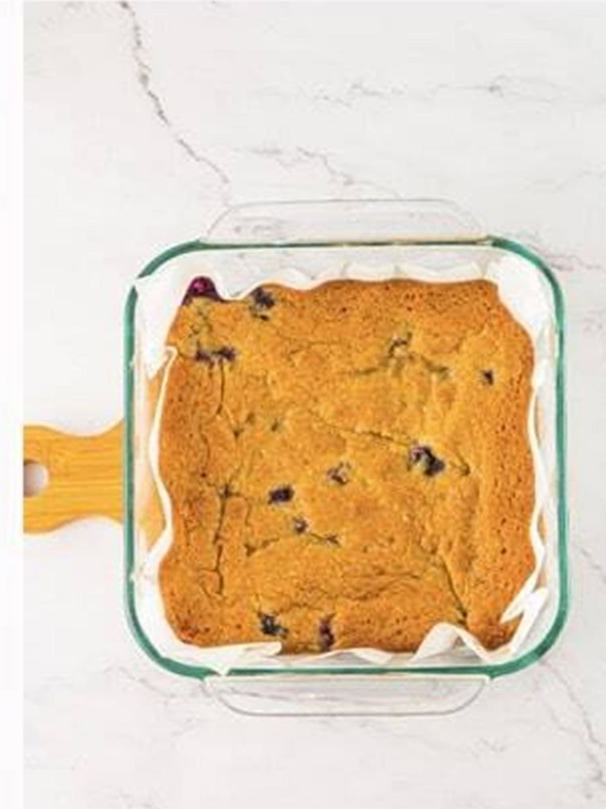 Golden baked white chocolate blondies with blueberries cooling in the glass baking pan.