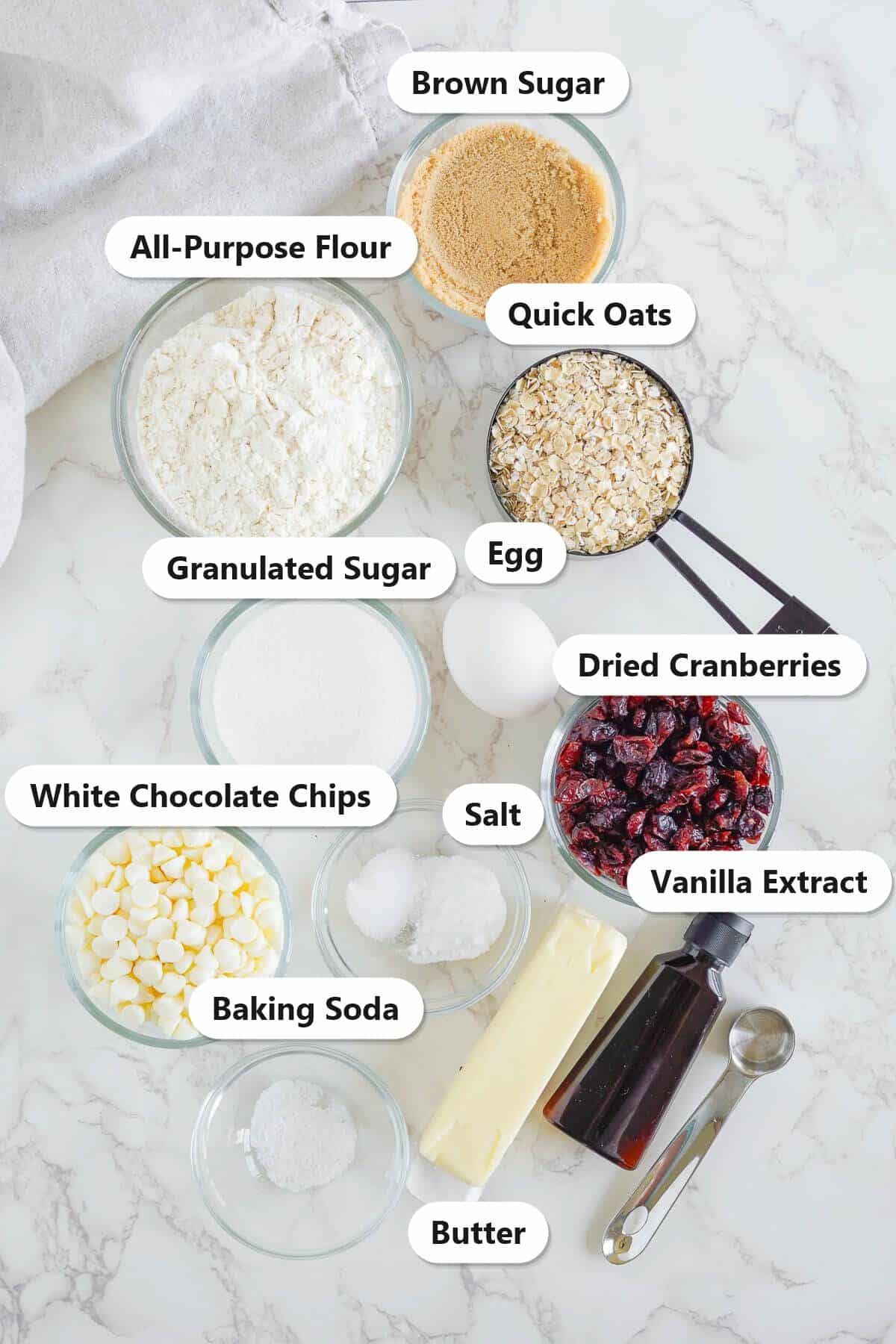 Labeled ingredients for White Chocolate Cranberry Cookies including flour, quick oats, dried cranberries, white chocolate chips, butter, and brown sugar.