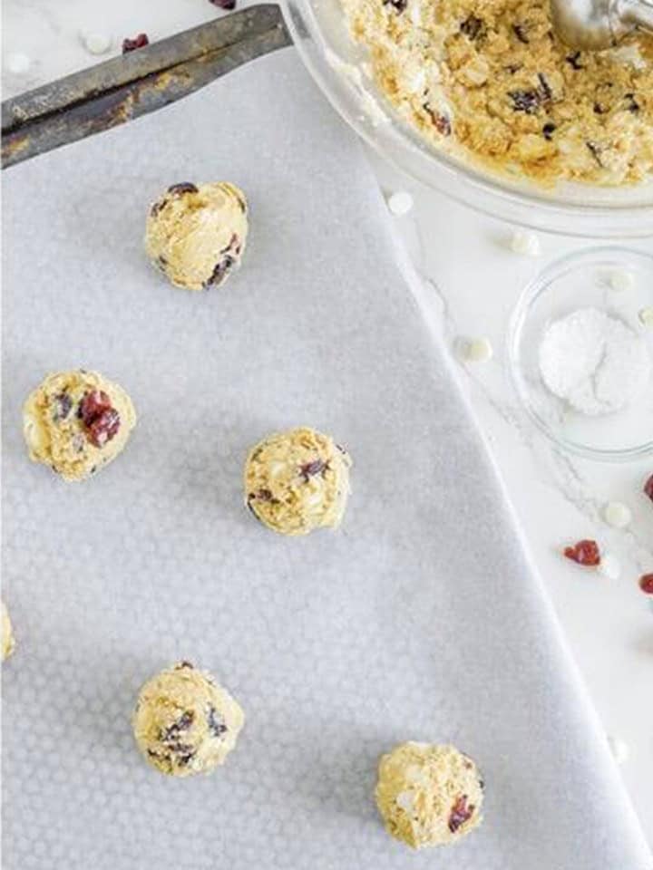 Scooped White Chocolate Cranberry Cookies dough balls on a parchment lined baking sheet.