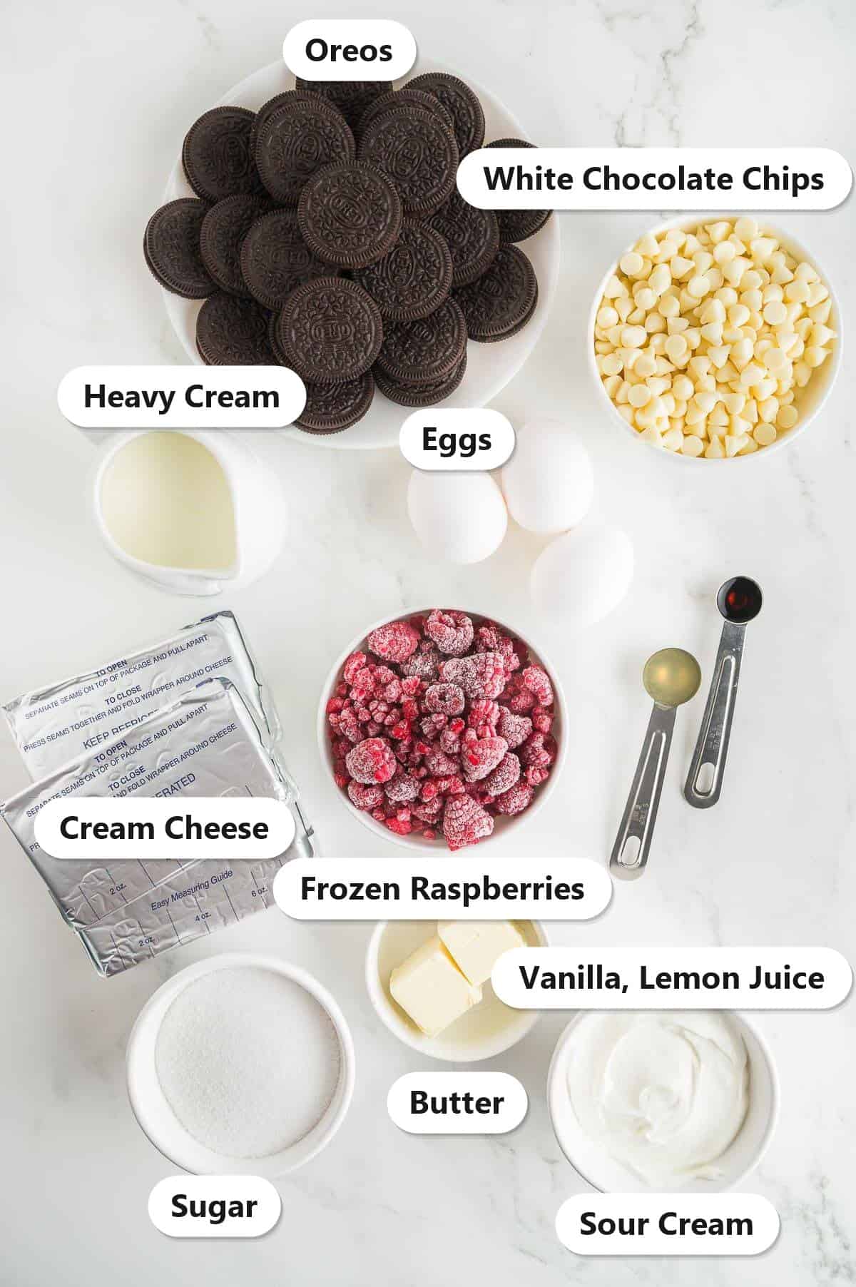 Labeled ingredients for White Chocolate Raspberry Cheesecake: Oreos, white chocolate chips, cream cheese, frozen raspberries, heavy cream, eggs, sugar, butter, sour cream, vanilla, and lemon juice.