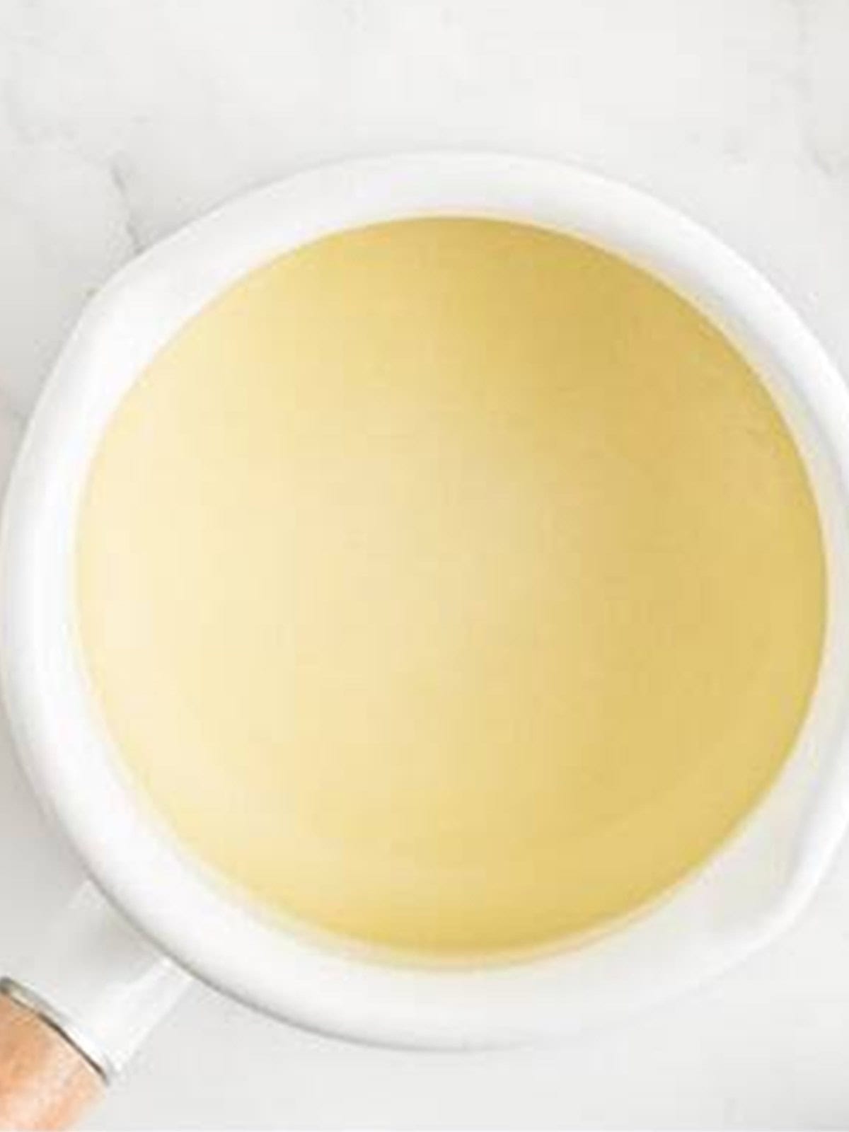 White chocolate chips melted with heavy cream in a saucepan for White Chocolate Raspberry Cheesecake.