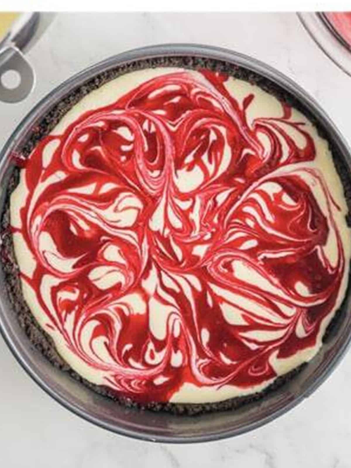 Raspberry sauce swirled into the cheesecake filling layers with a knife in the springform pan.