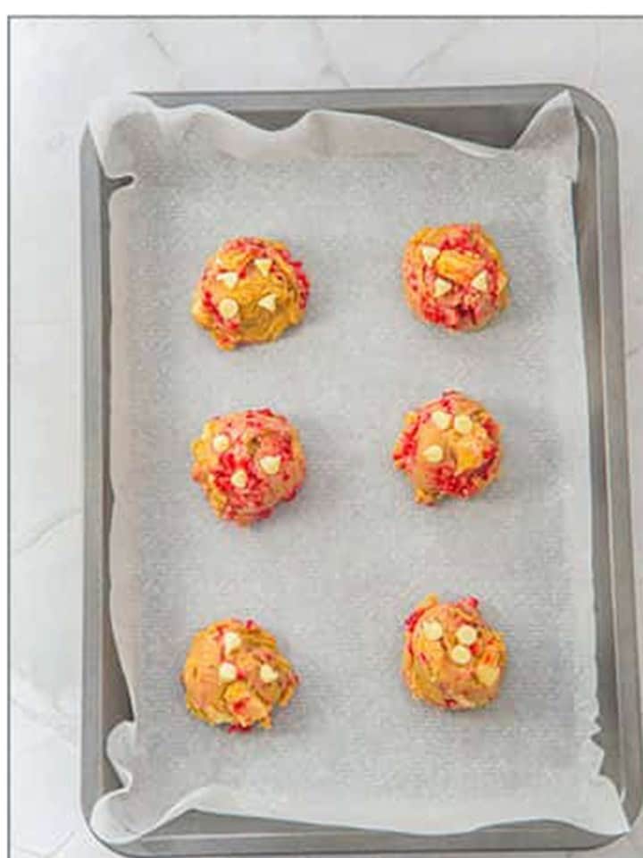 Cookie dough balls spaced out on a parchment lined baking sheet for White Chocolate Raspberry Cookies.