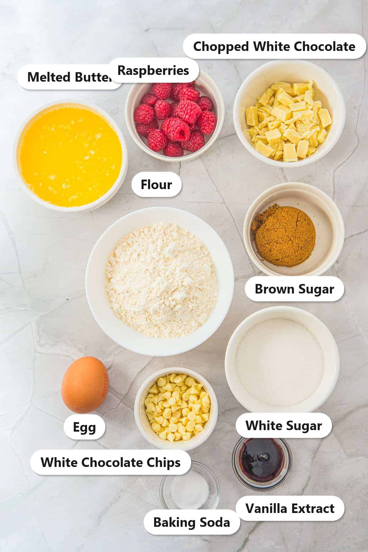 Labeled ingredients for White Chocolate Raspberry Cookies: flour, melted butter, raspberries, chopped white chocolate, white chocolate chips, brown sugar, white sugar, egg, vanilla, and baking soda.