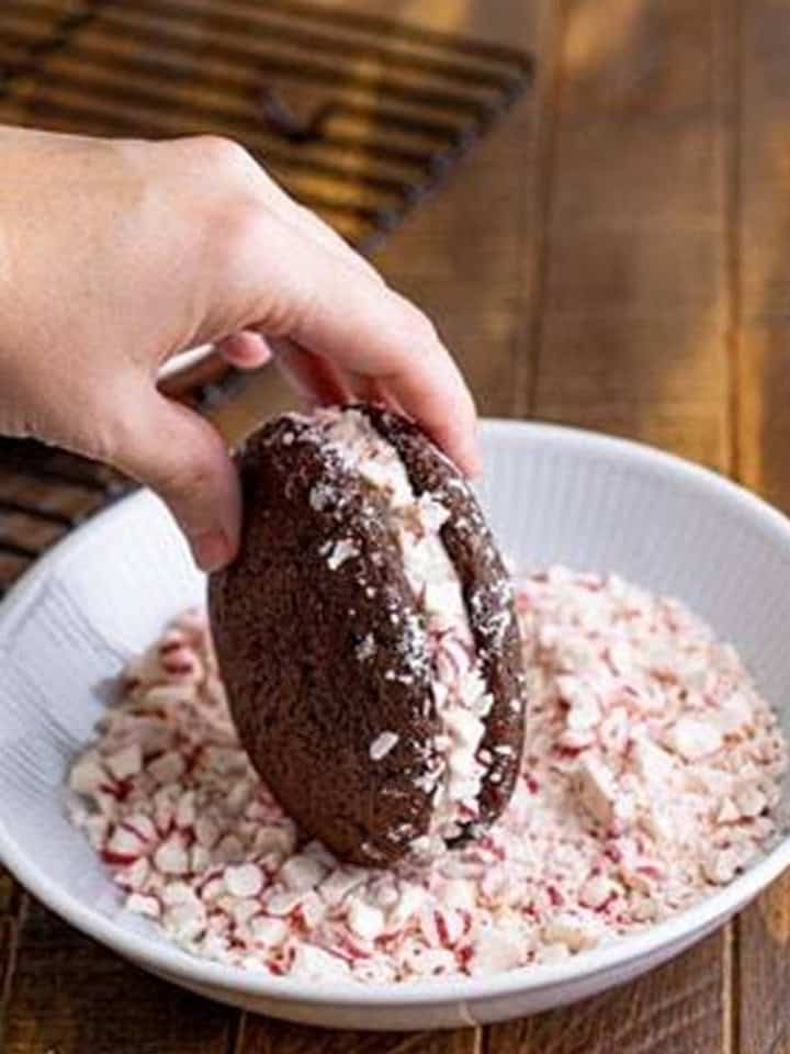 Filled whoopie pie being rolled in crushed peppermints so they stick to the filling.