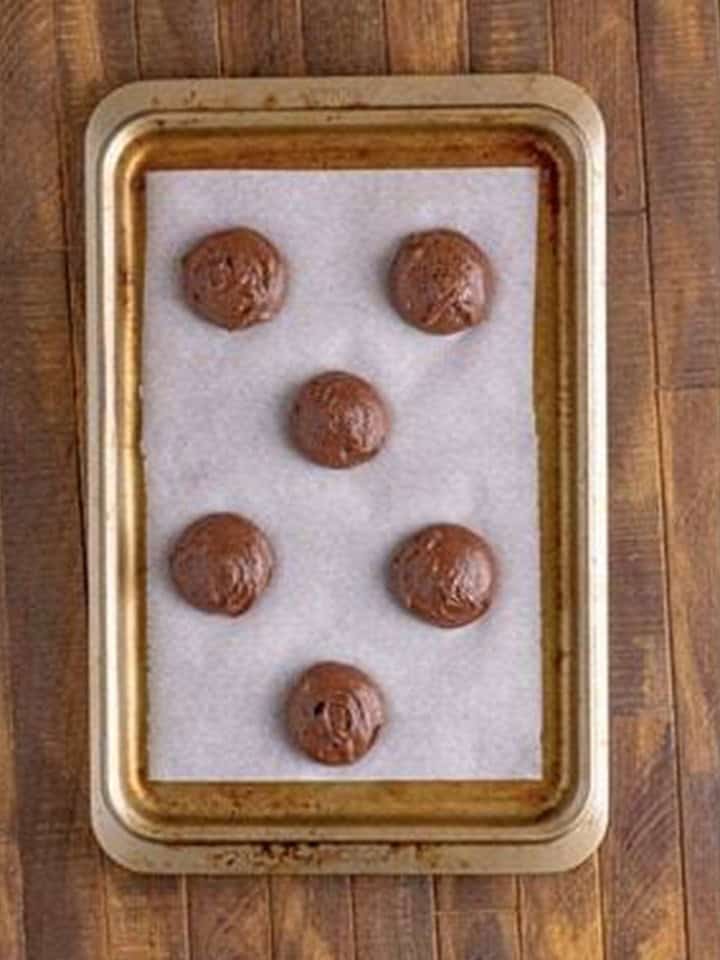Dollops of chocolate Whoopie Pies batter scooped onto a parchment lined sheet tray.