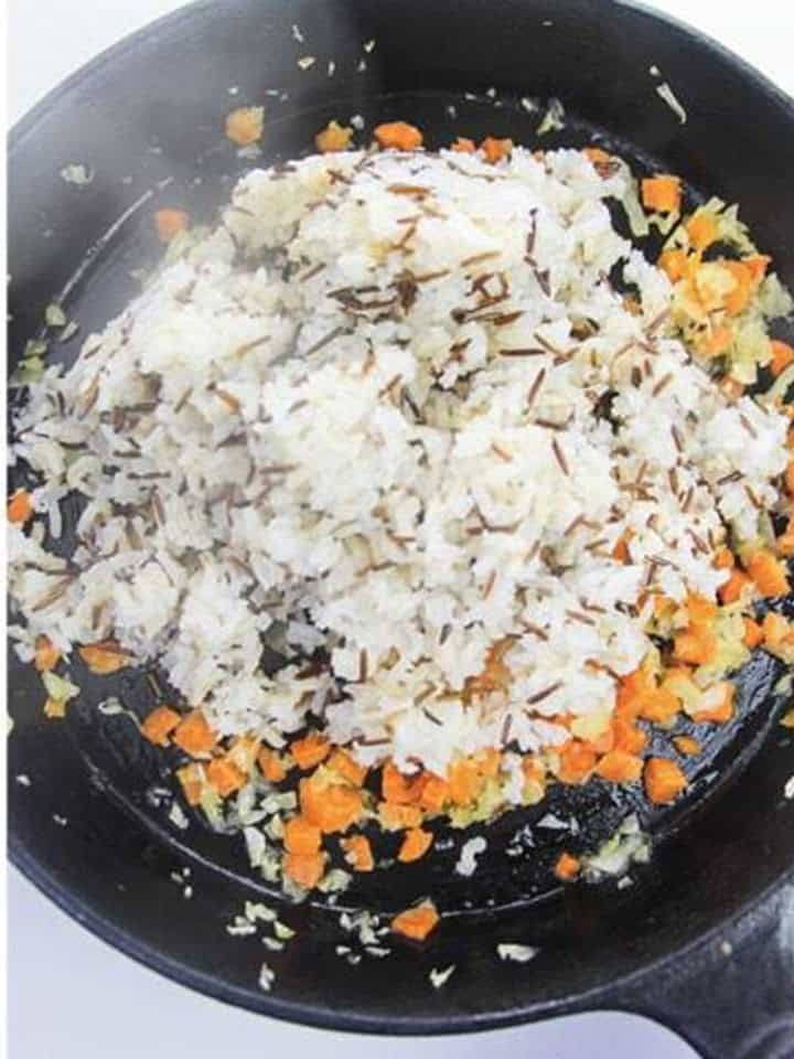 Adding the cooked wild rice blend to the skillet of sauteed vegetables.