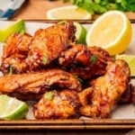 Crispy air fryer chicken wings tossed in honey sriracha glaze piled on a platter with lemon and lime wedges.