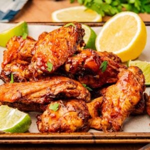 Crispy air fryer chicken wings tossed in honey sriracha glaze piled on a platter with lemon and lime wedges.