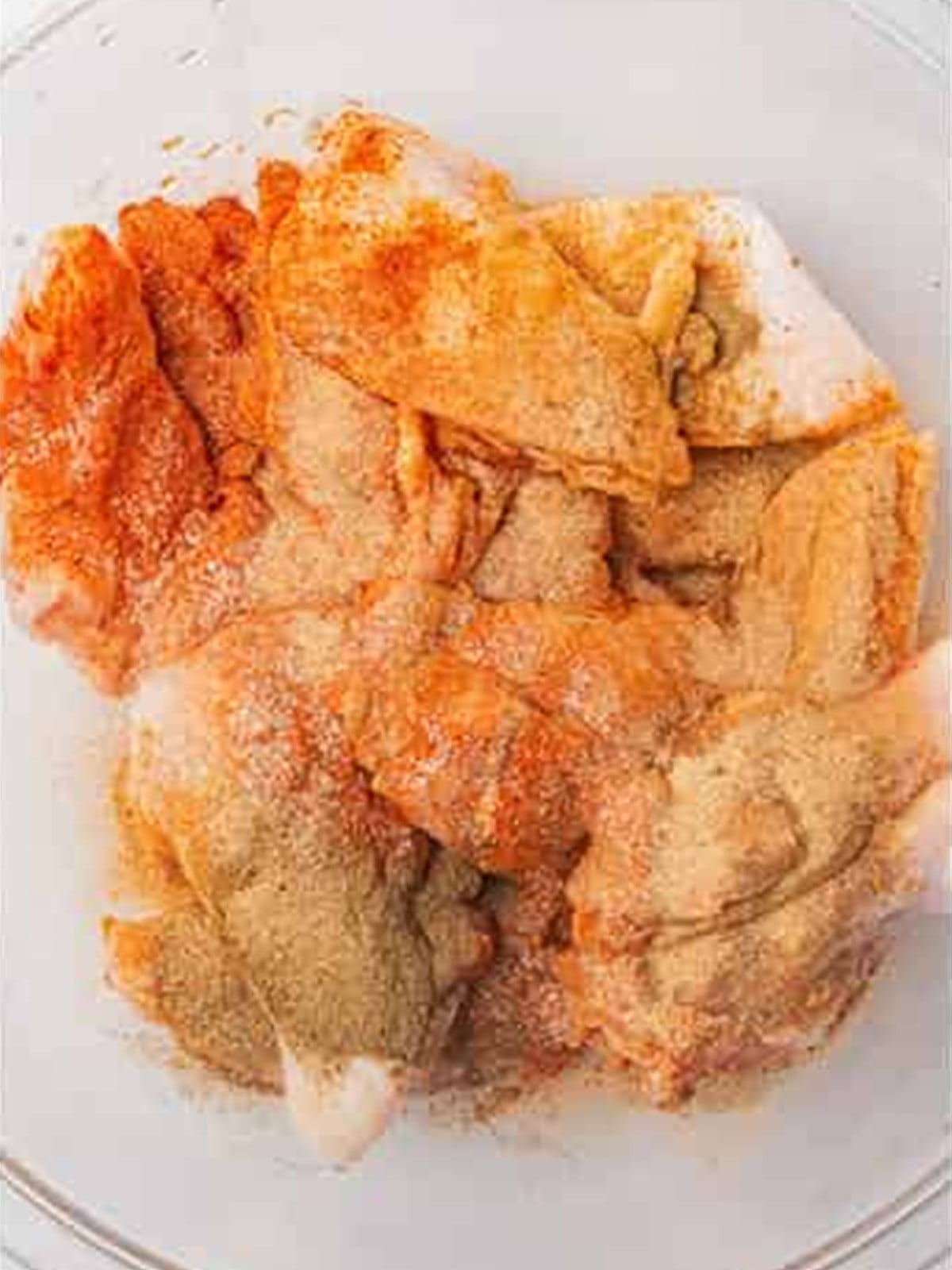 Raw chicken wings in a glass bowl sprinkled with salt, black pepper, garlic powder, and smoked paprika.