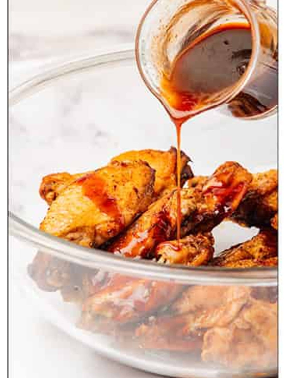 Honey sriracha glaze being poured over crispy air fryer chicken wings in a glass bowl.