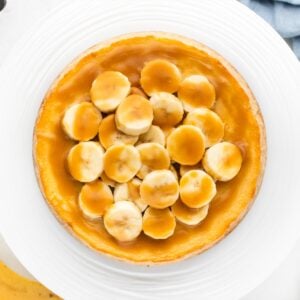 Banoffee cheesecake on a cake stand with toffee sauce poured over the top and banana slices on the edge.