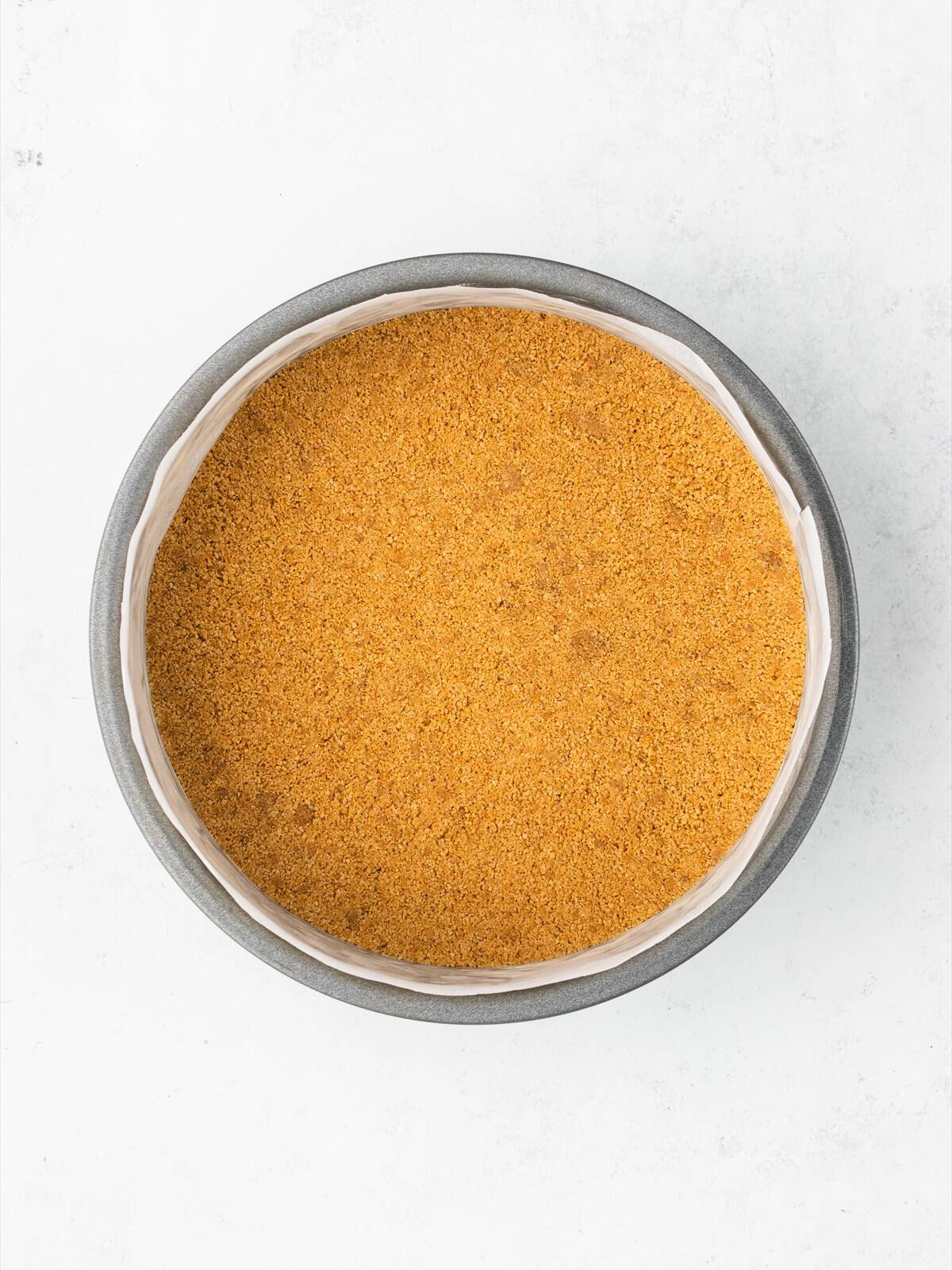 The graham cracker crumb mixture pressed into an even compacted layer in the bottom of a lined cake pan.
