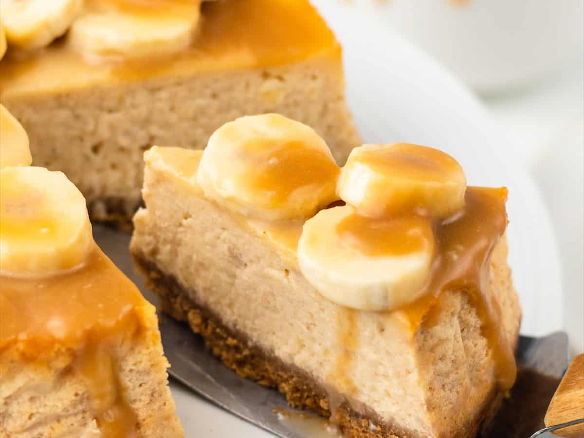 A slice of banoffee cheesecake on a plate showing the graham cracker base, creamy banana filling and toffee topping.