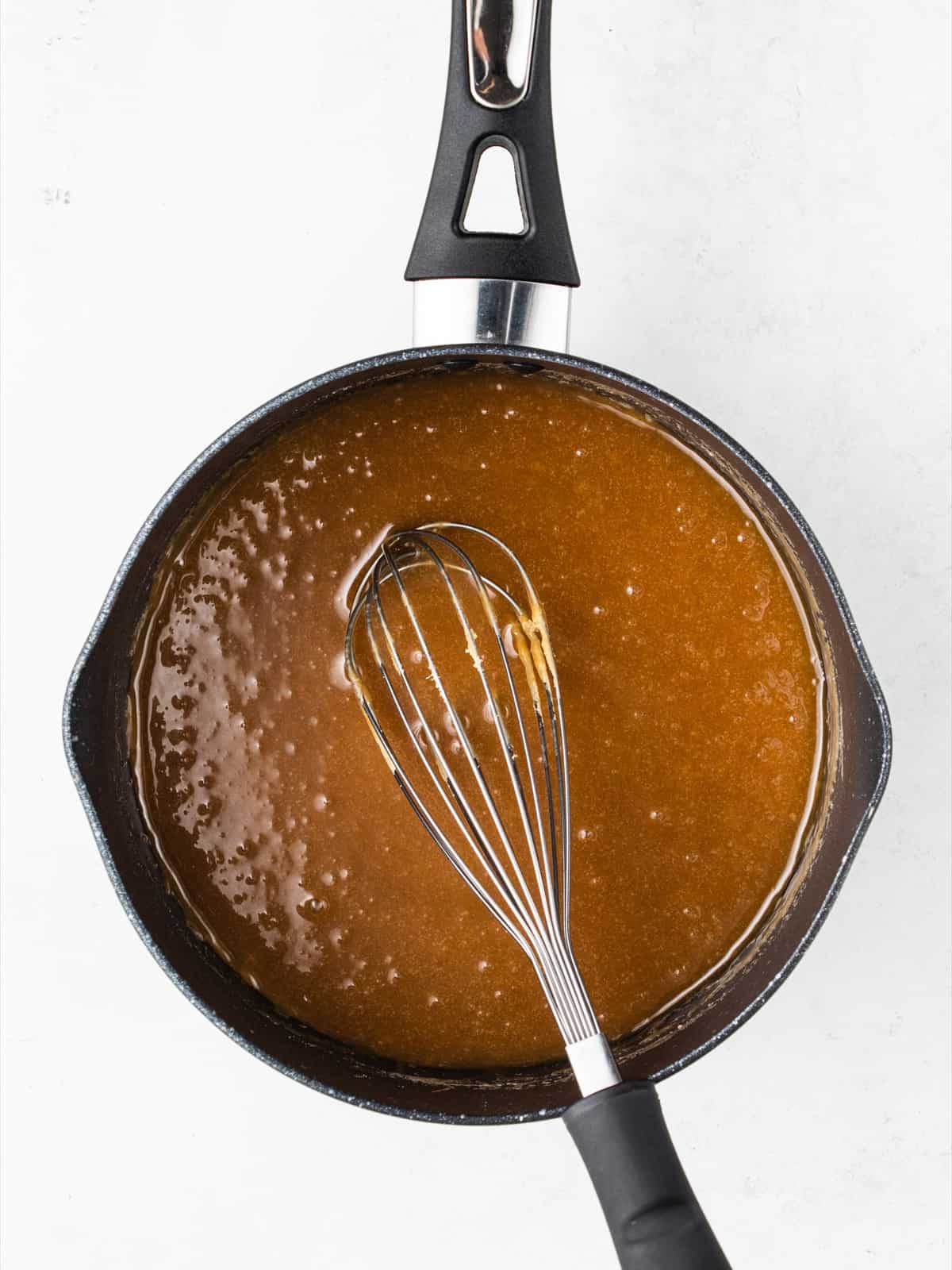Homemade toffee sauce being poured over the top of the cooled banoffee cheesecake.