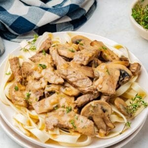 Classic beef stroganoff with tender sirloin strips and mushrooms served over egg noodles on a white plate.
