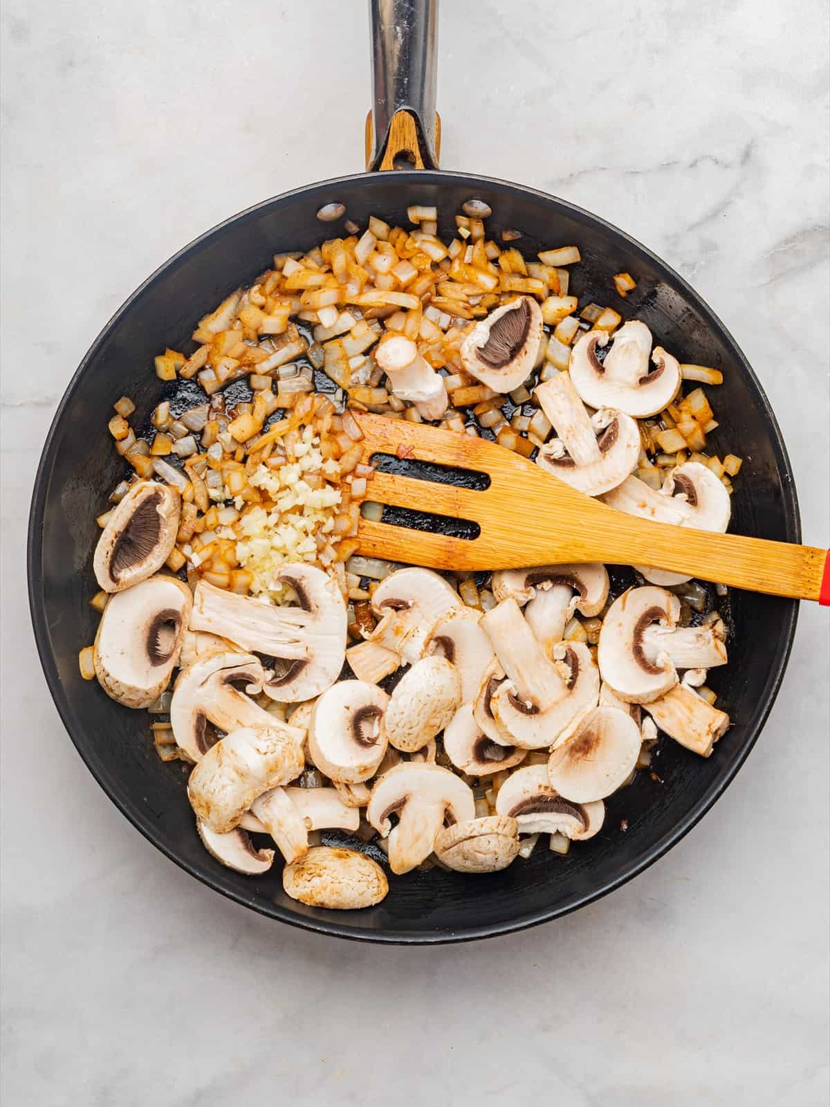 Minced garlic and sliced cremini mushrooms added to the buttery onions in the skillet.