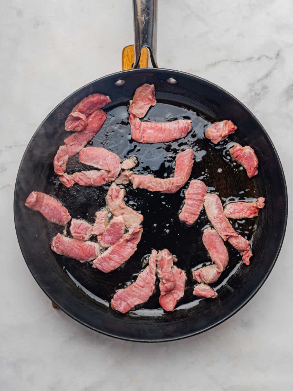 Seasoned sirloin strips laid into a hot skillet with olive oil for beef stroganoff.