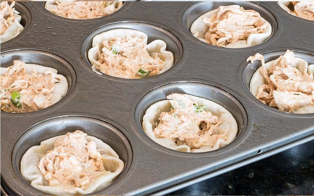 Tortilla cups in a muffin tin filled with creamy chicken enchilada mixture.