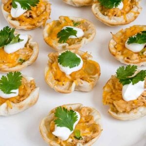 Chicken enchilada bites garnished with sour cream and cilantro on a white platter.