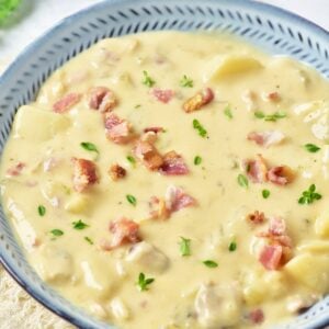 Creamy New England clam chowder in a blue rimmed bowl topped with crumbled bacon and fresh parsley.