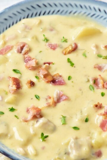 Creamy New England clam chowder in a blue rimmed bowl topped with crumbled bacon and fresh parsley.