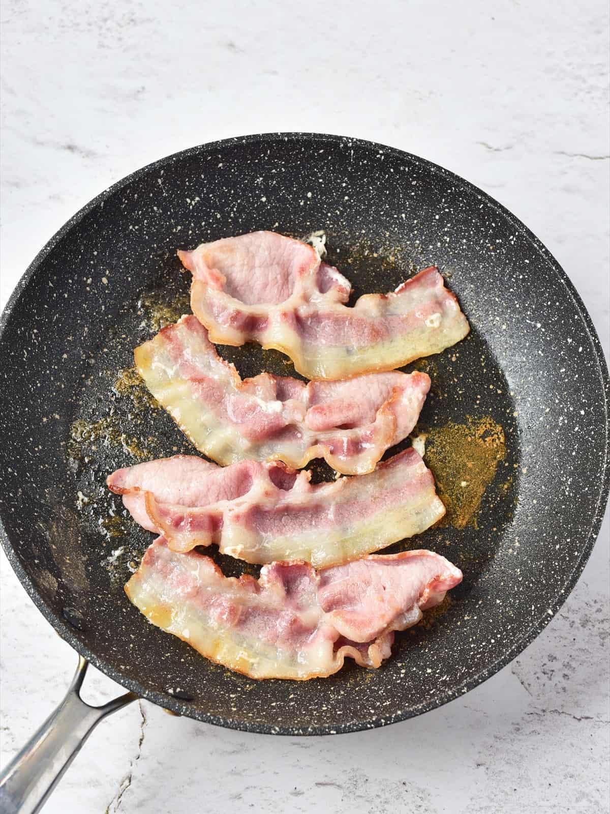 Strips of bacon frying in a dry skillet for clam chowder.