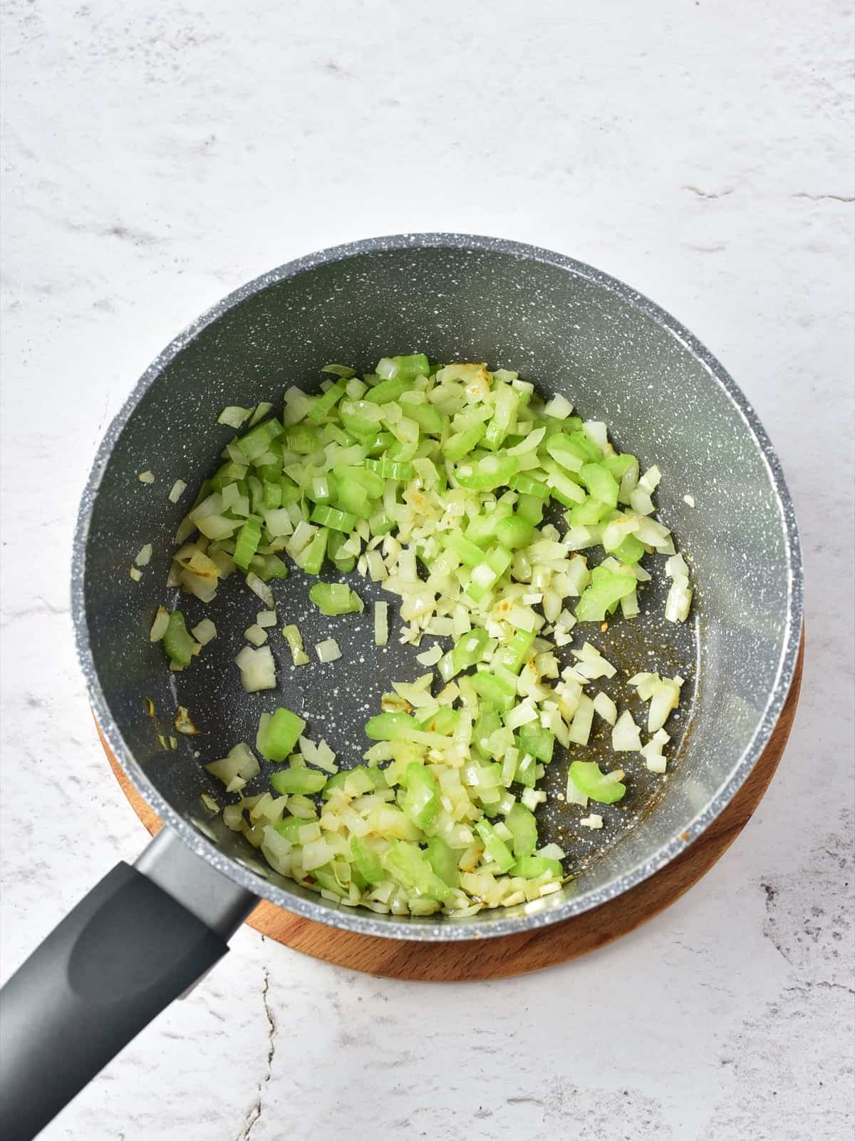 Chopped onion and celery softening in olive oil in a saucepan for clam chowder.