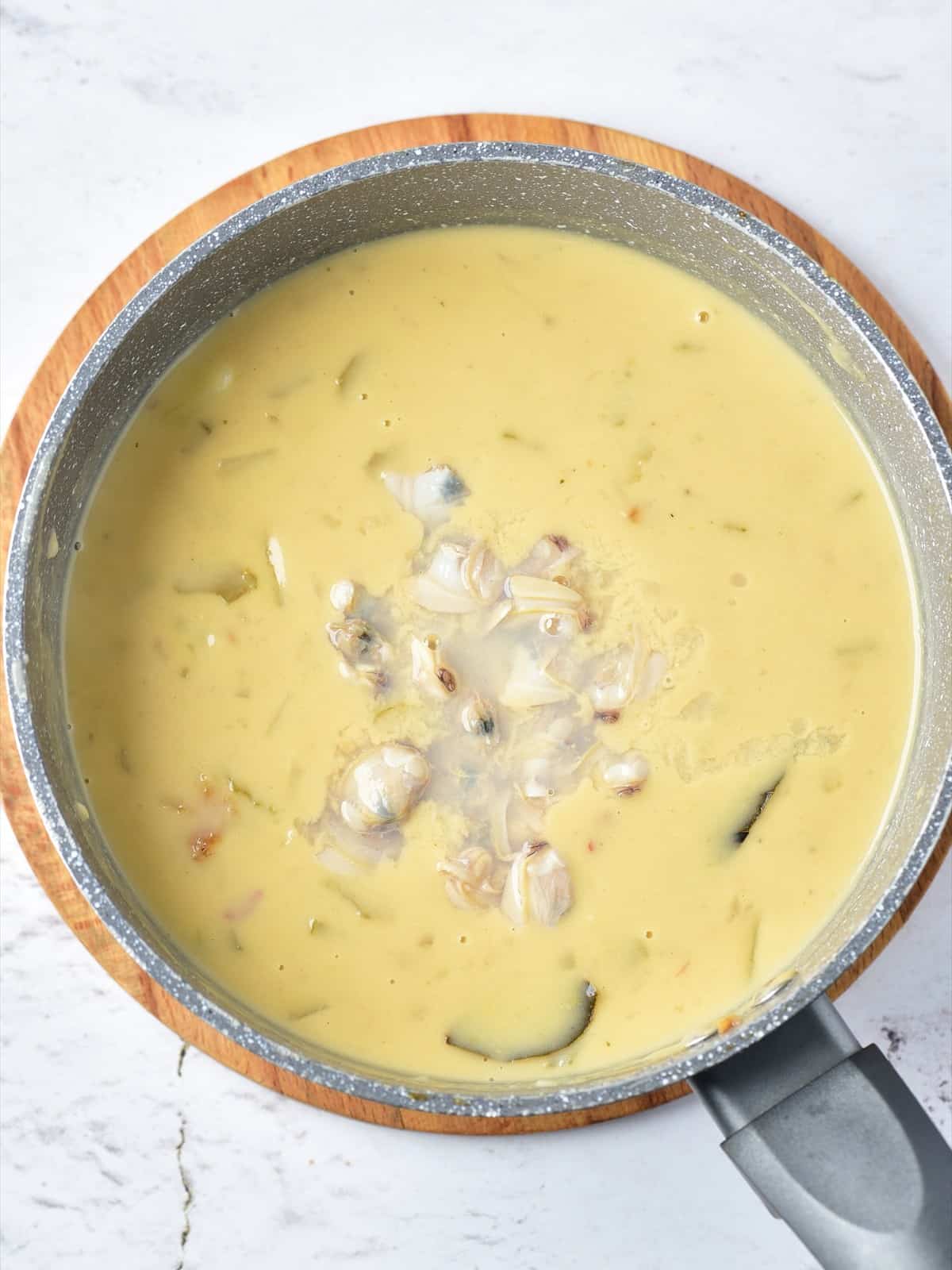 Shucked clams stirred into the finished creamy clam chowder in a saucepan.