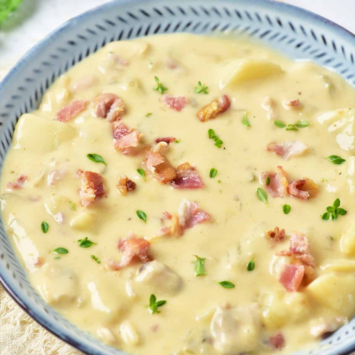 Creamy New England clam chowder in a blue rimmed bowl topped with crumbled bacon and fresh parsley.