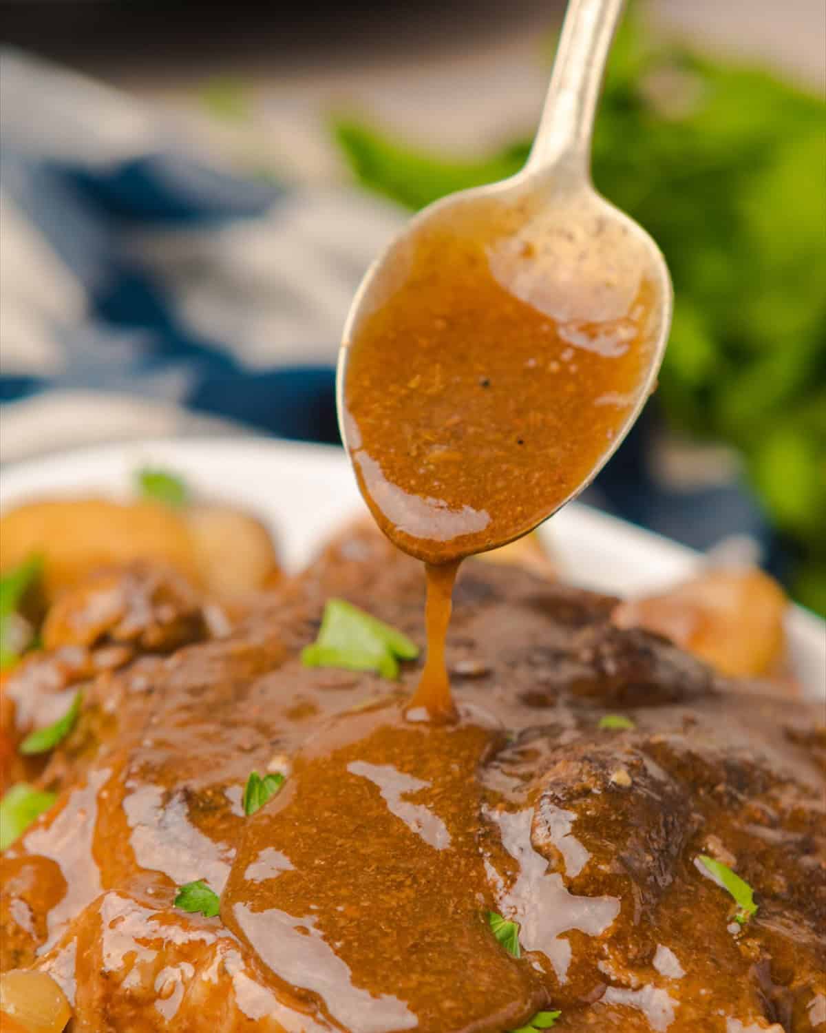 Brown gravy being spooned over a crock pot pot roast on a serving platter.