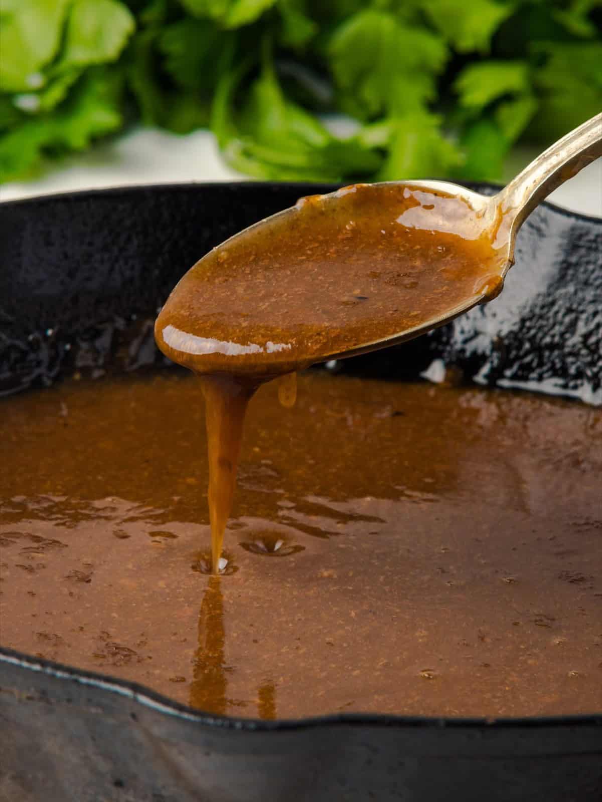 Thickened pot roast gravy coating the back of a spoon over a skillet.
