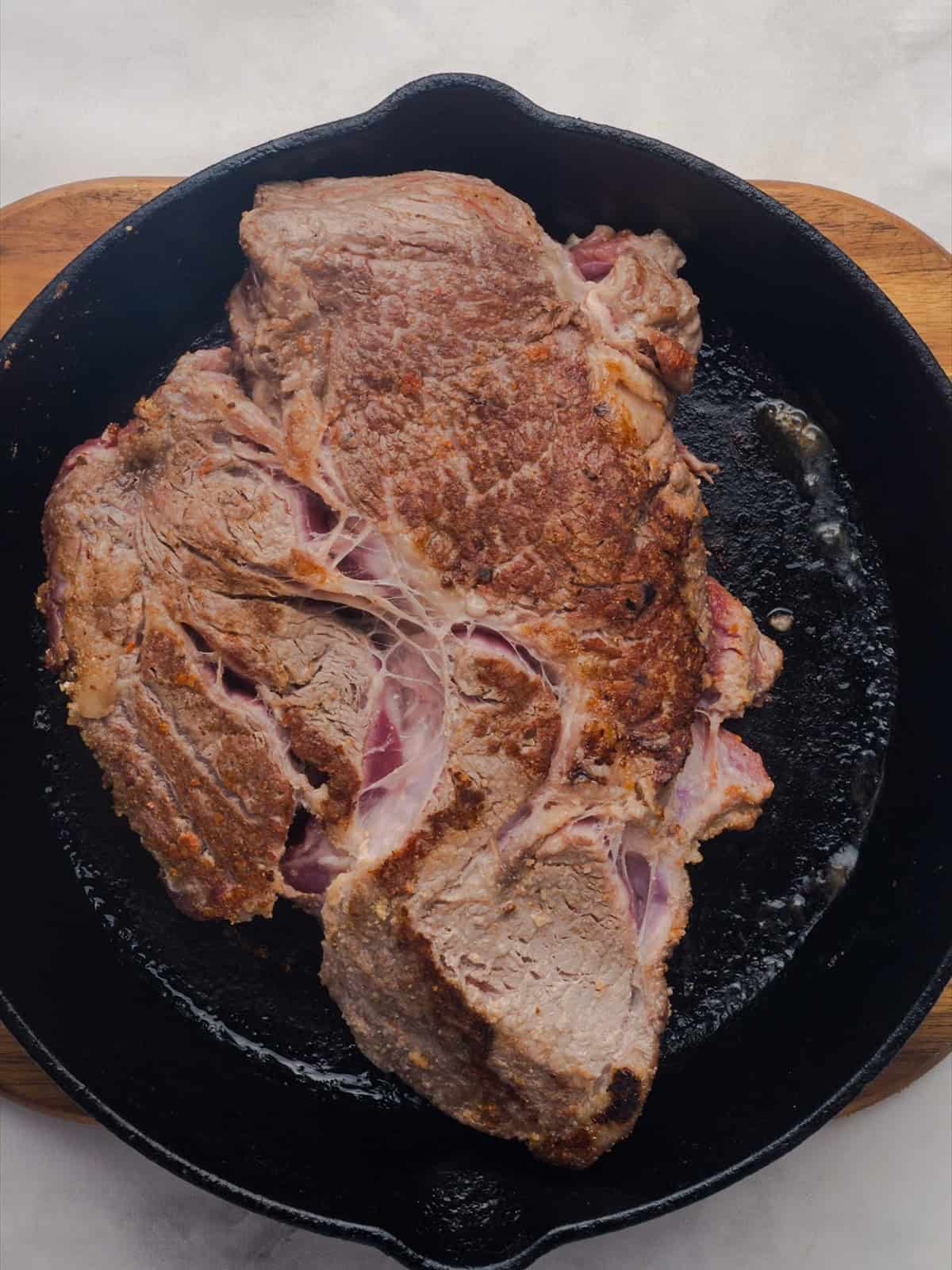Seasoned chuck roast searing in a cast iron skillet for crock pot pot roast.
