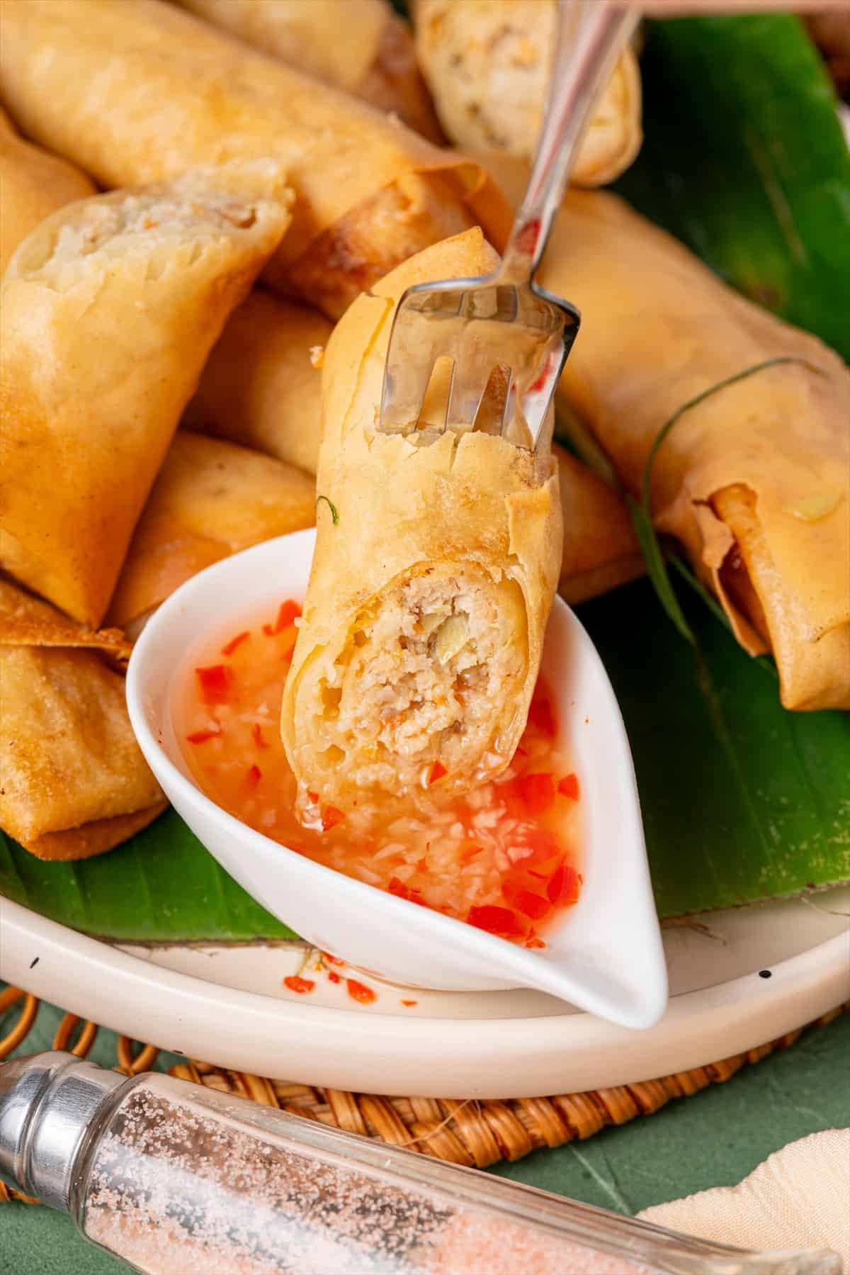 A fork dipping a crispy Filipino lumpia into sweet chili sauce
