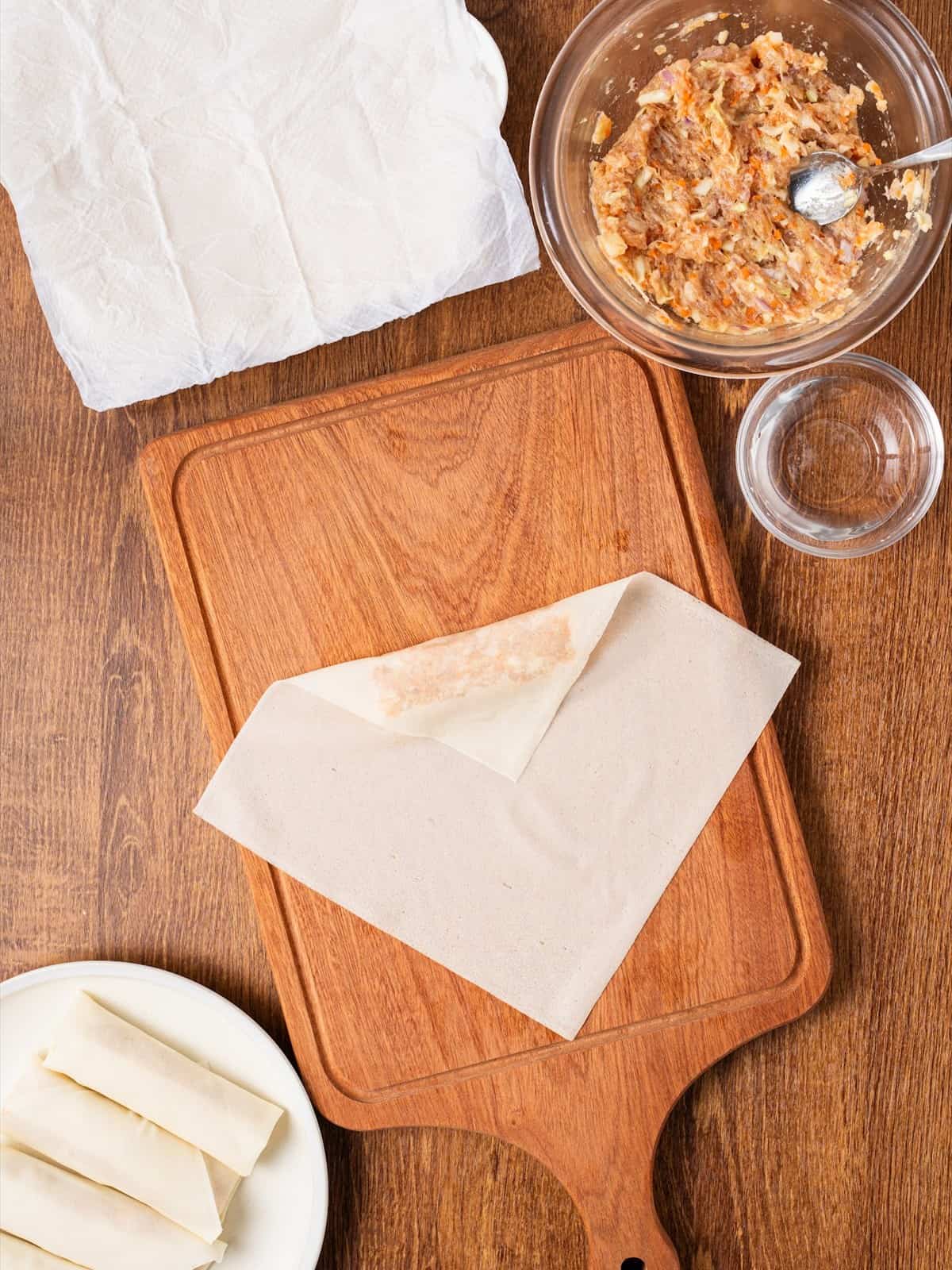 Folding the top corner of a lumpia wrapper over the pork filling