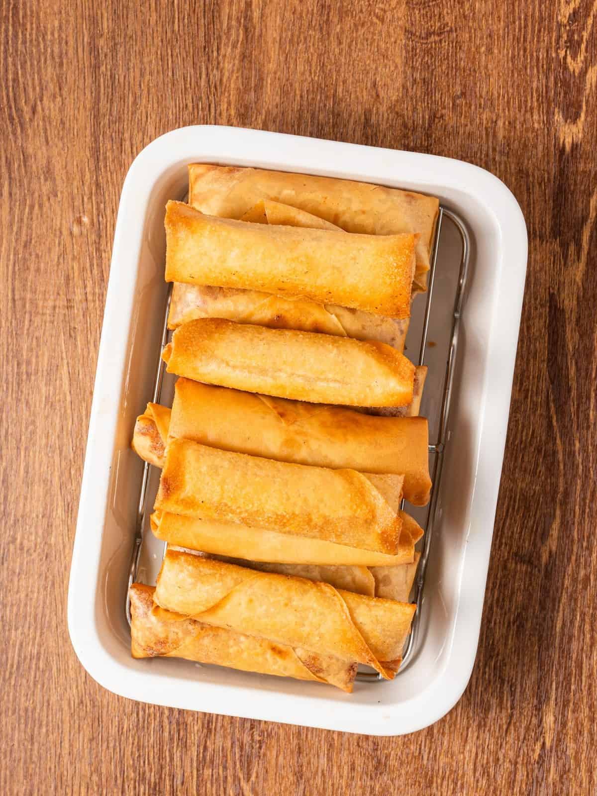 Golden fried Filipino lumpia draining on a rack set in a white tray