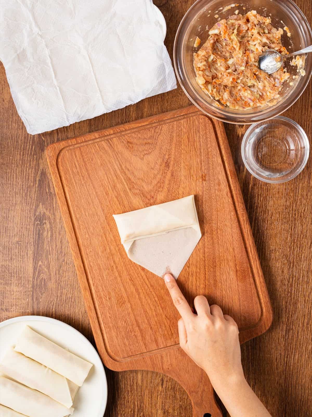 Hands folding the sides of a lumpia wrapper in toward the center before rolling